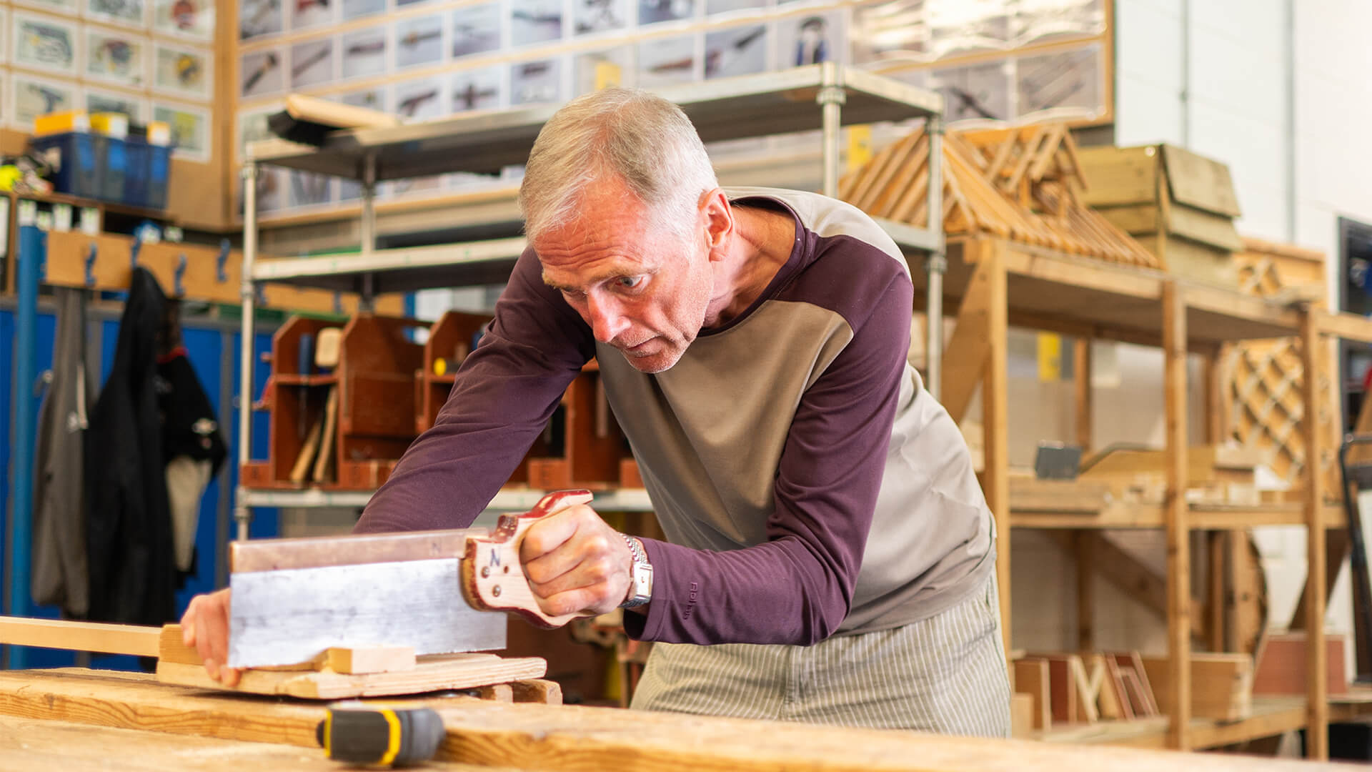 Man leaning over bench sawing block of wood.