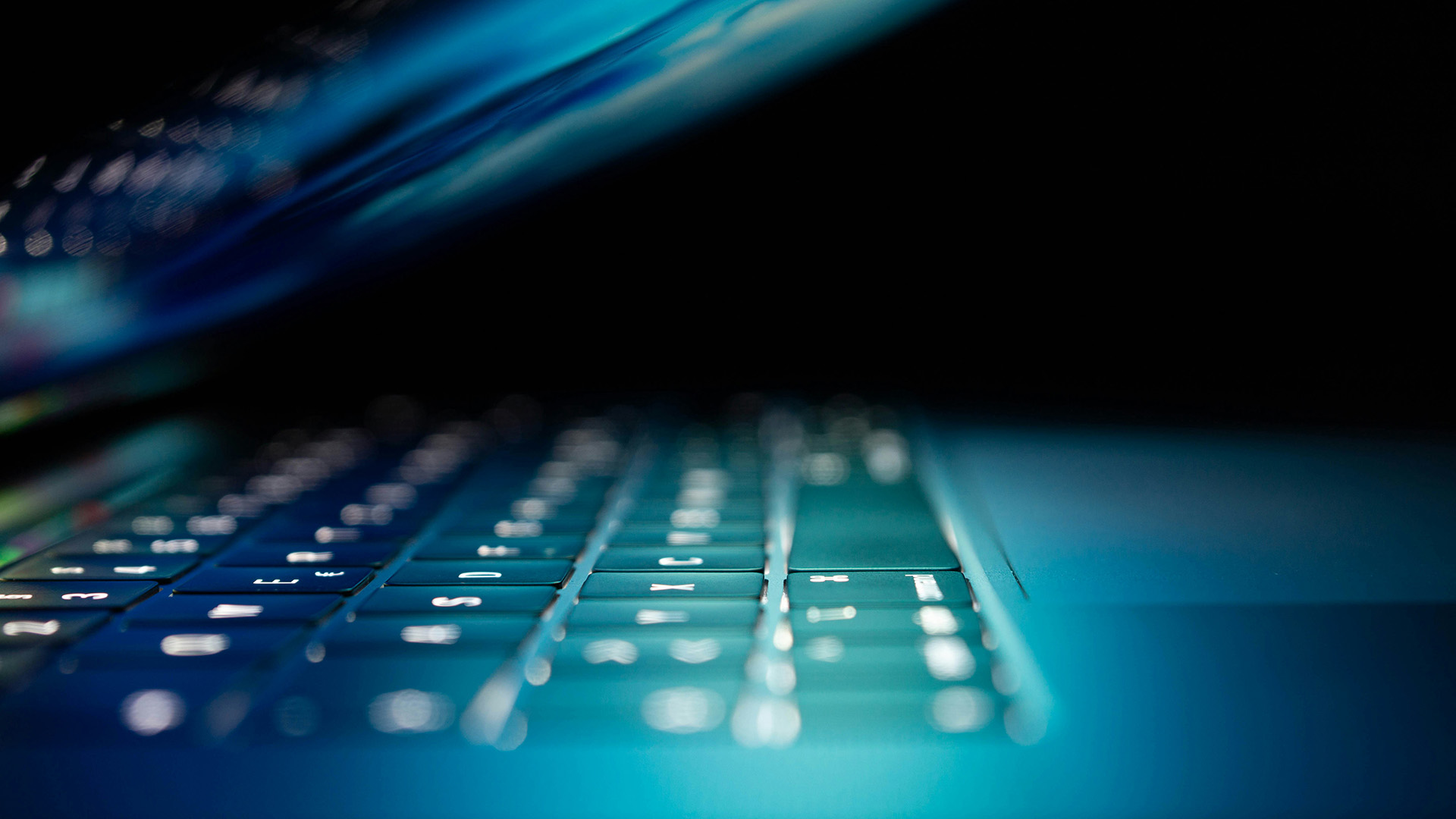 Close up of half-closed laptop with screen lit up shining on keyboard