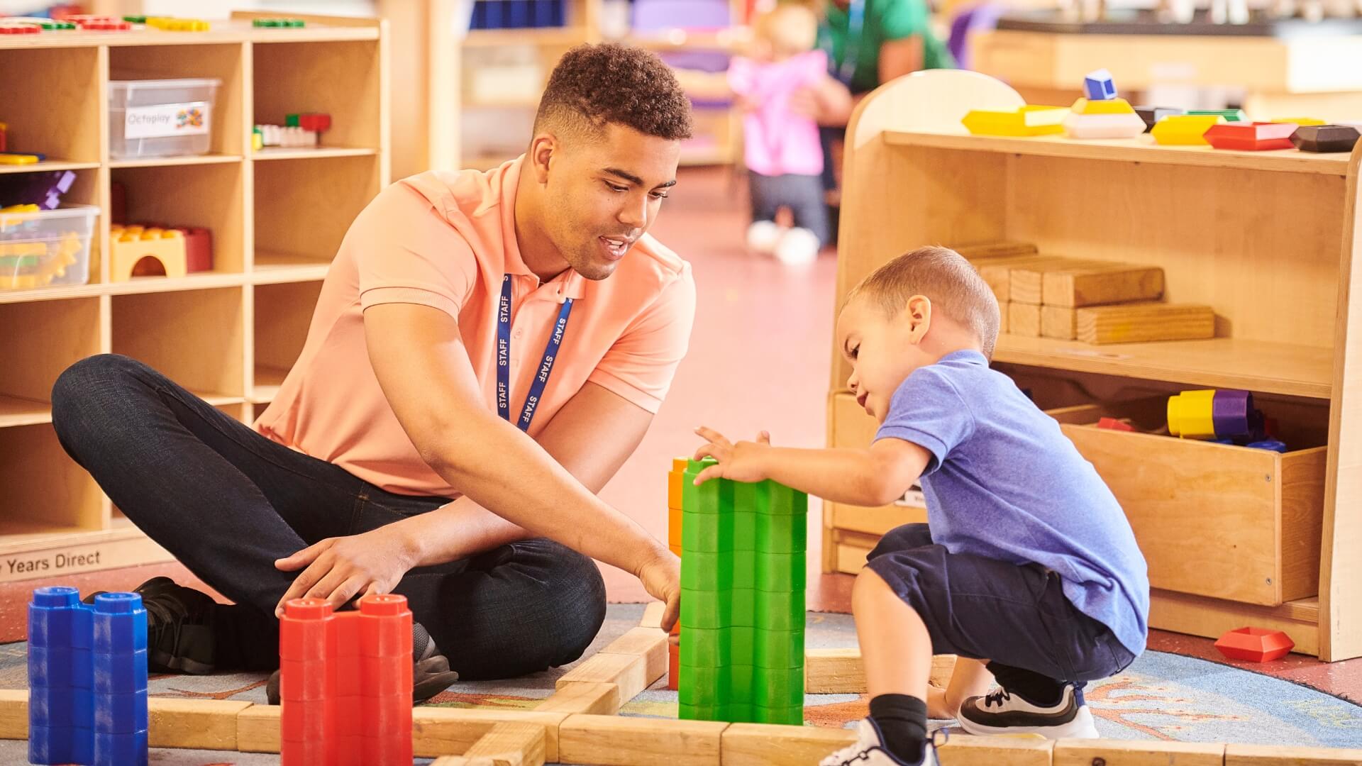 Nursery nurse sat on a nursery floor with small children.