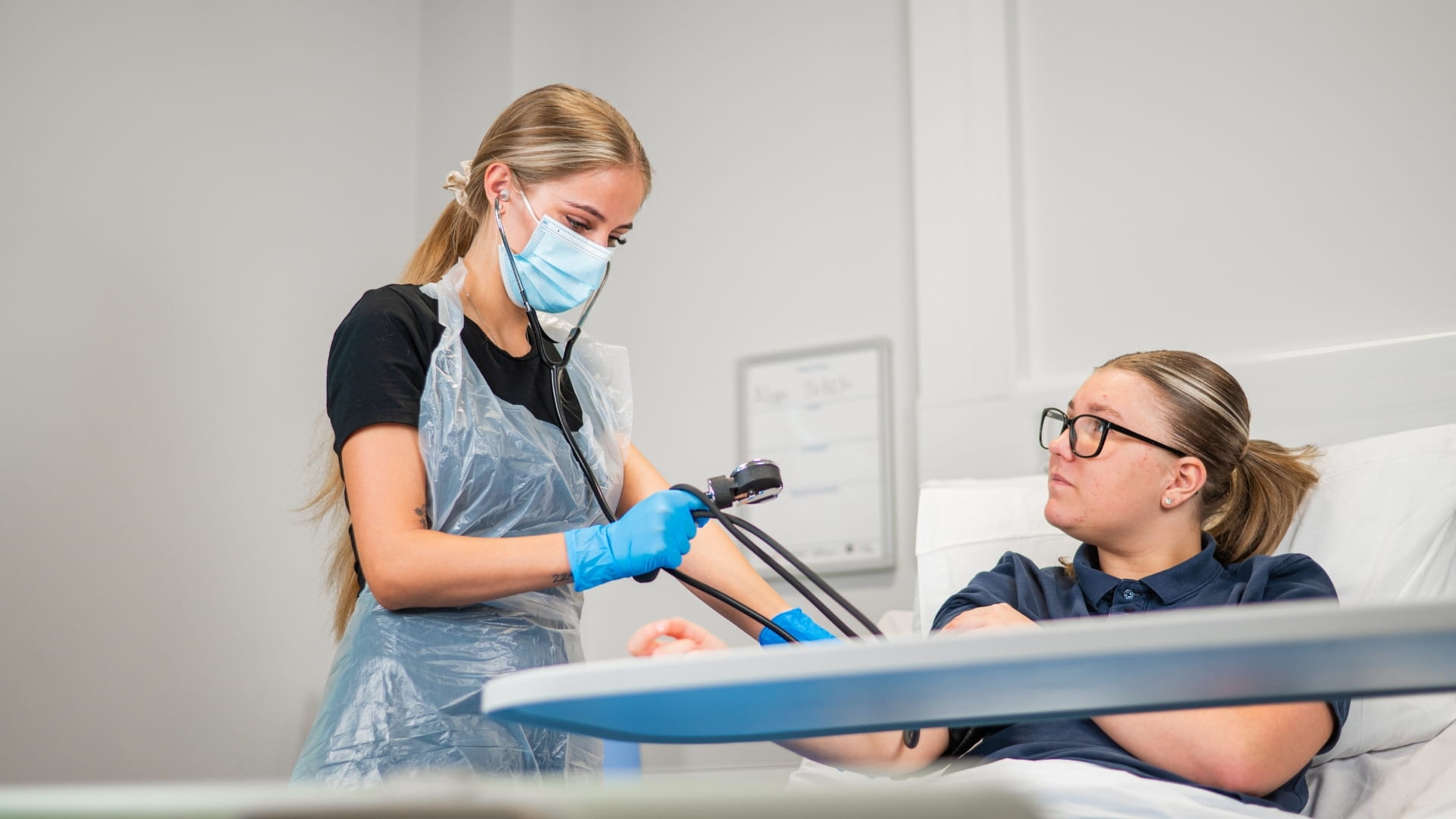 Care student wearing apron and mask using a blood pressure monitor