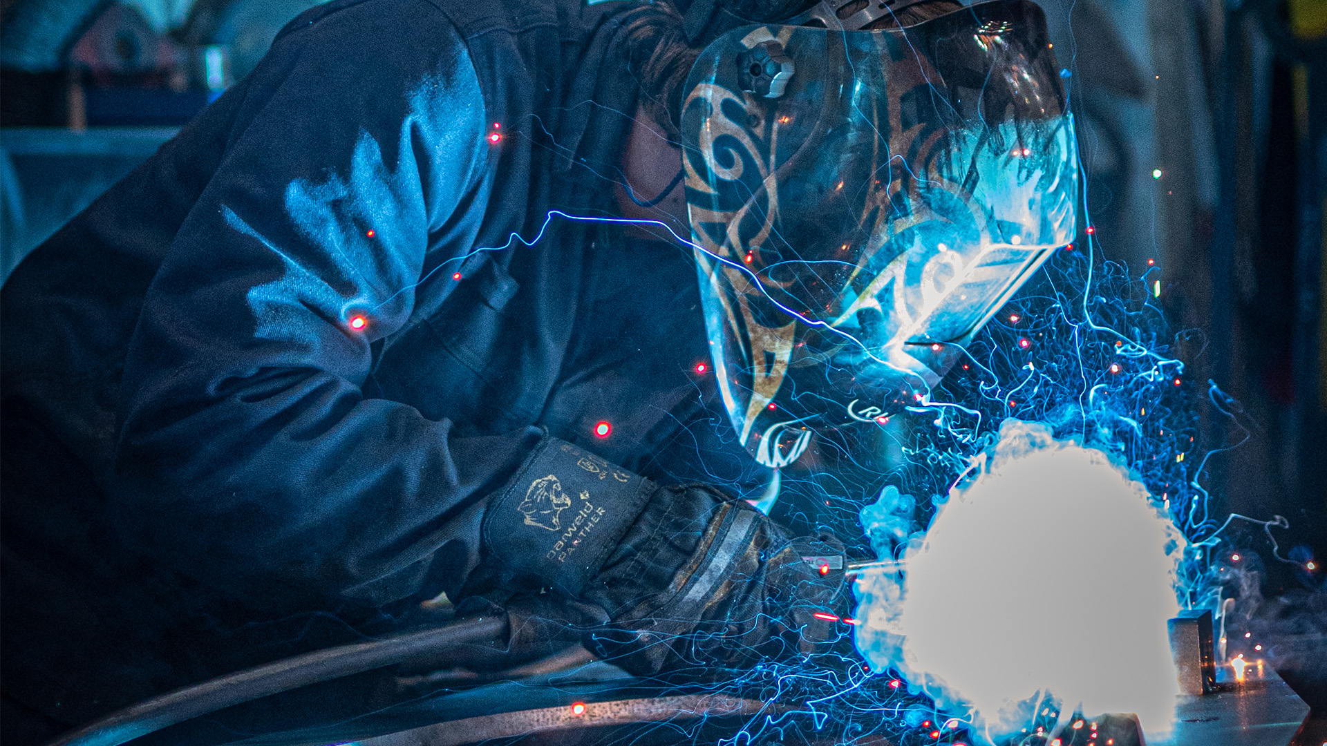 Person wearing mask welding with blue sparks flying