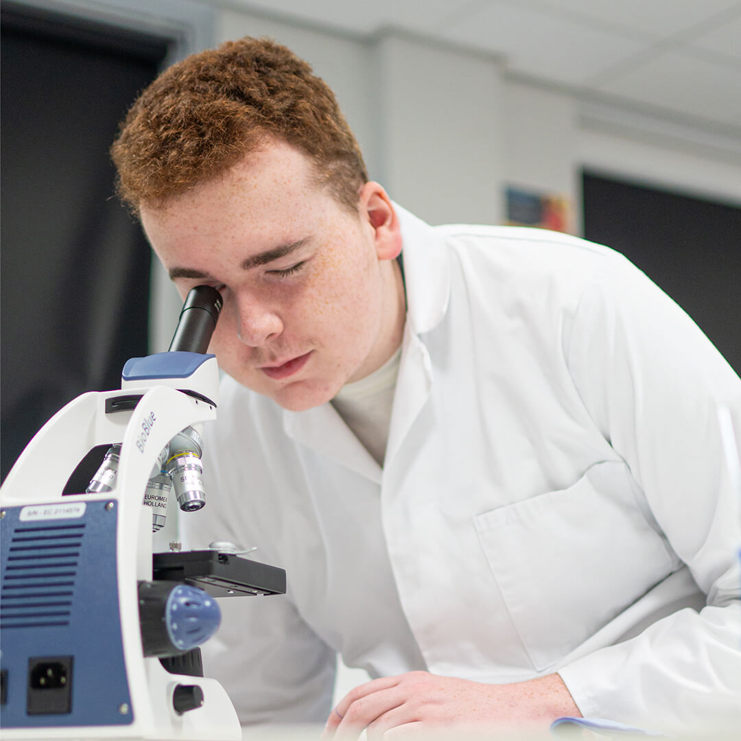 Young man in classroom using microscope.