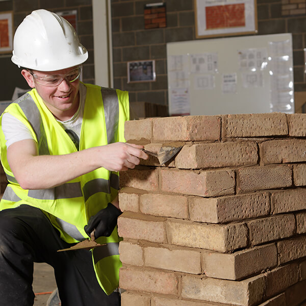 Young man wearing a hard hat and high-vis jacket, working on a stack of bricks.