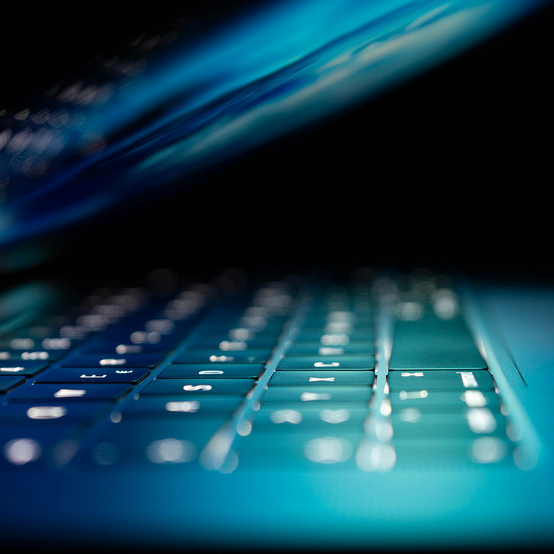 Close up of half-closed laptop with screen lit up shining on keyboard