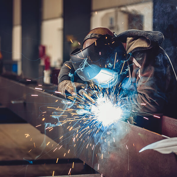 Welder wearing a safety mask and welding a metal bar.