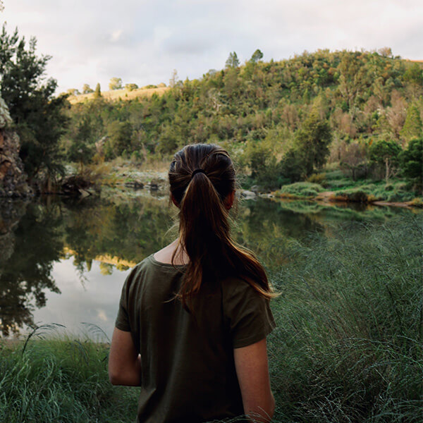 Young woman standing by a beautiful landscape of trees, shrubs and a lake.