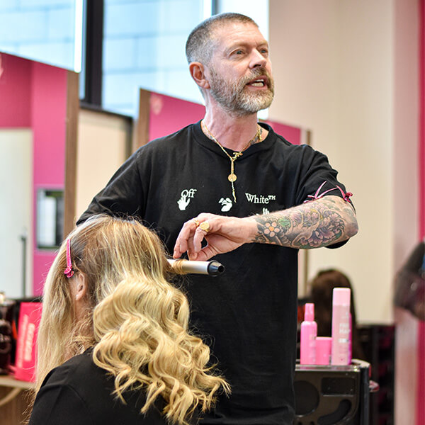 Celebrity hair stylist, Lee Stafford, curling a blonde woman's hair whilst in East Durham College's hair salon.