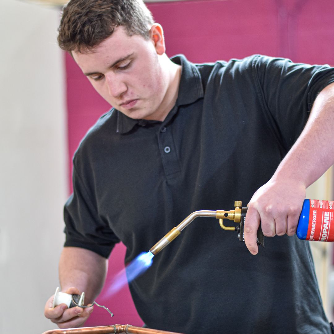 A man holding a blowtorch working on some copper pipes.