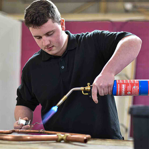 A man holding a blowtorch working on some copper pipes.