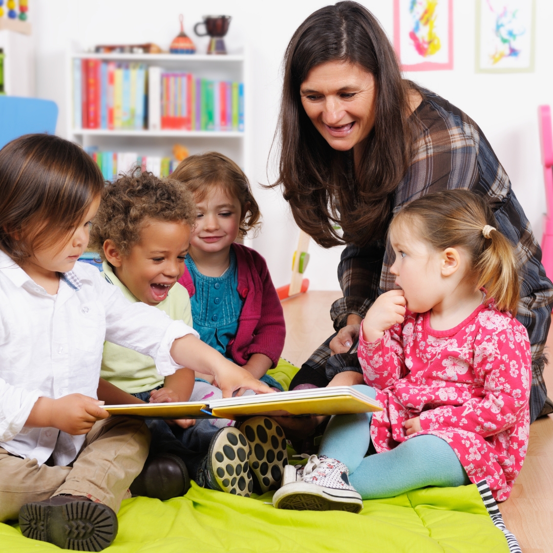 Two nursery nurses playing with small children outside. The children are playing on hoppers and trampolines.