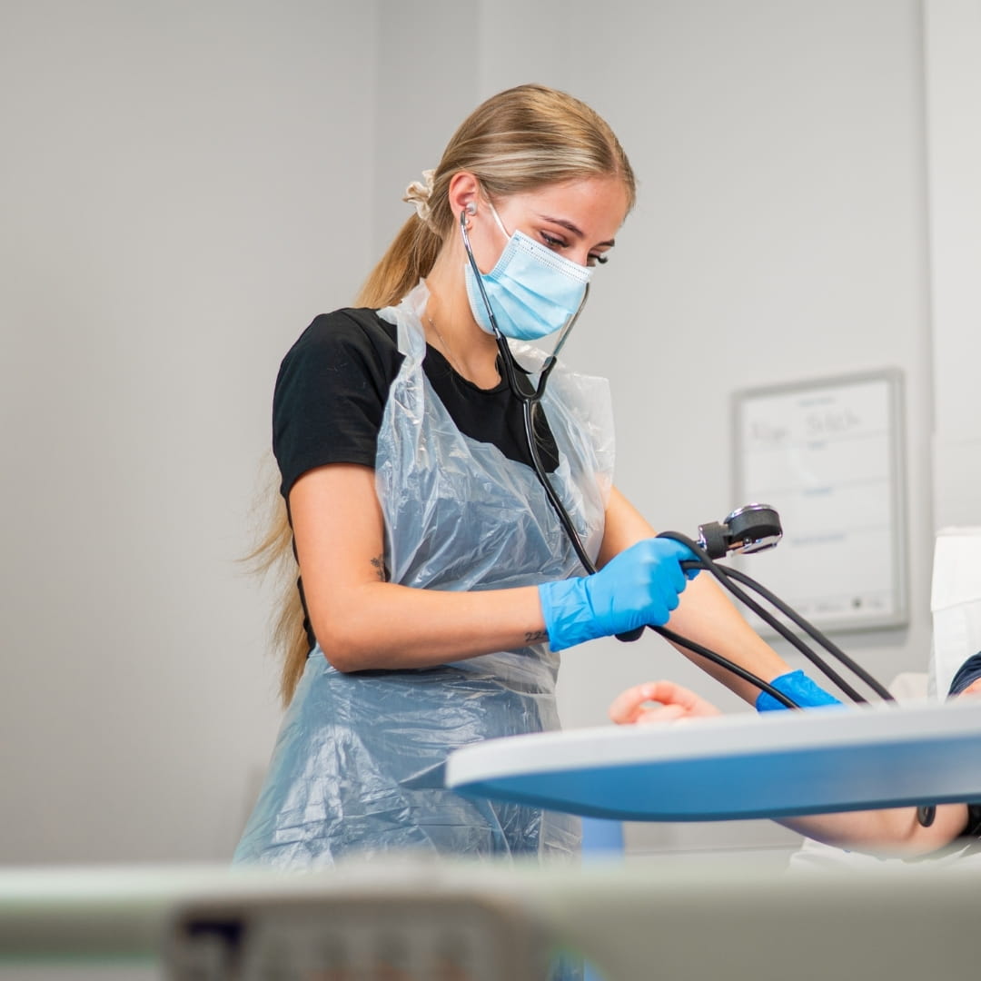 Care student wearing apron and mask using a blood pressure monitor