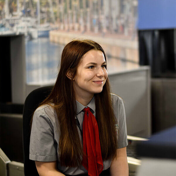 A young woman wearing a travel agents uniform sat at a desk and smiling.