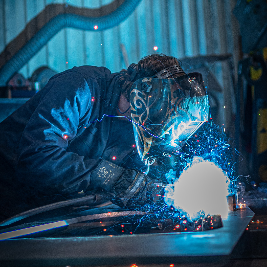 Person wearing mask welding with blue sparks flying