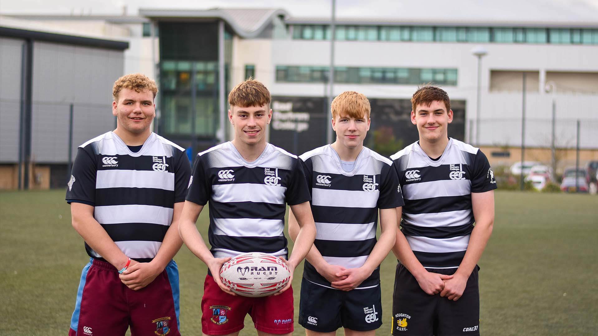 Four rugby students smiling at camera with a building behind them