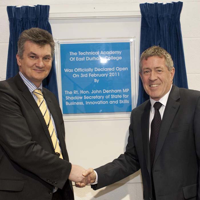Two people shaking hands with a plaque behind them