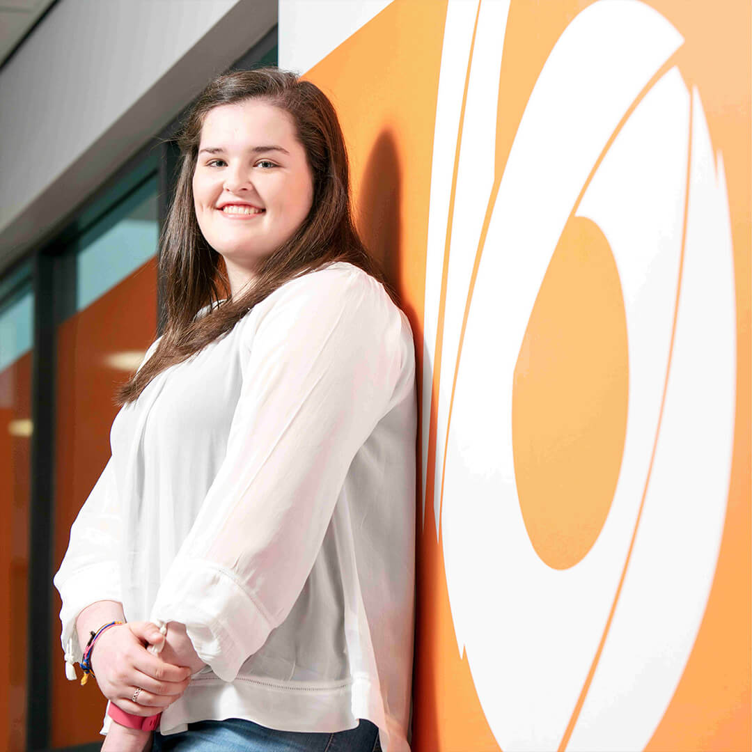 A woman smiling and leaning on an orange wall