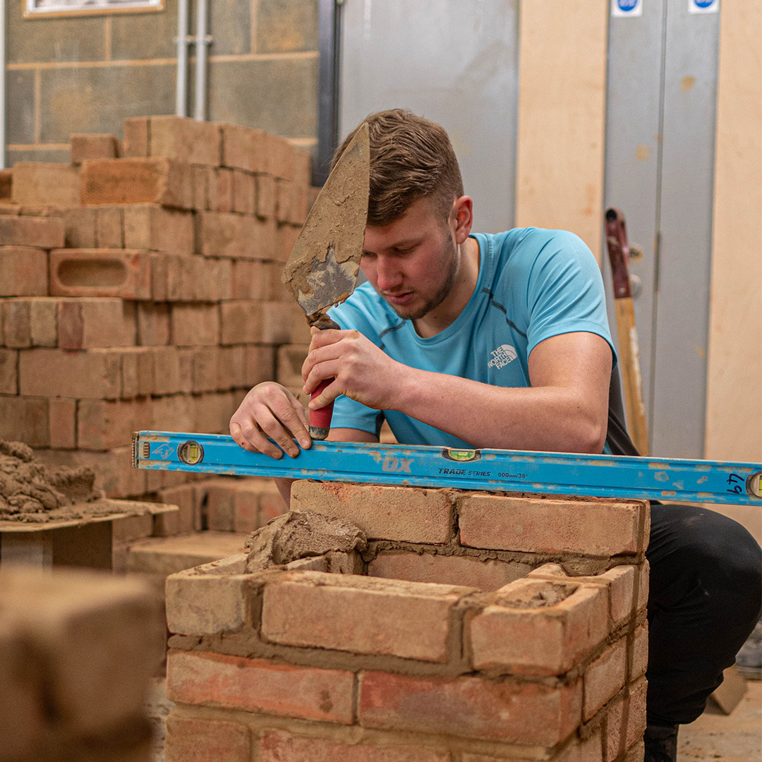 Bricklaying student using spirit level on brick pile