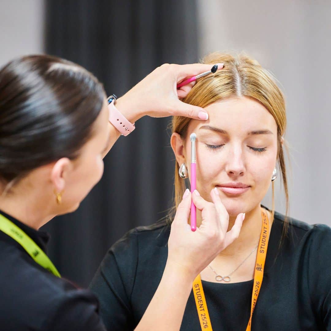 Beauty lecturer applying eye makeup to student
