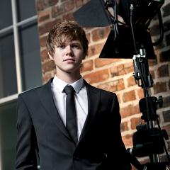 Student in a business suit stood next to lighting rig and brick wall