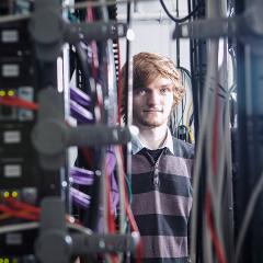 Student in stripy shirt stands in between server equipment