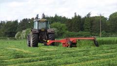 A tractor cutting a grass field with a red cutter