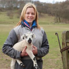 Former student Shelly Whitfield stood in a field holding a lamb