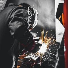 Engineer in welding mask and boiler suit creating sparks