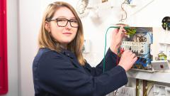 Teenage girl wearing glasses looking at the camera and testing circuitry in an electrical board