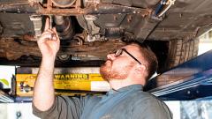 Man wearing glasses examining the underside of a car