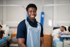 Smiling male student in hospital gown in front of hospital beds