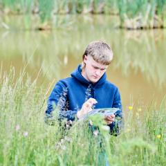 Student standing in tall grass looking at paper