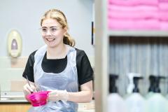 Hairdressing student wearing apron smiling and holding colour mixing bowl